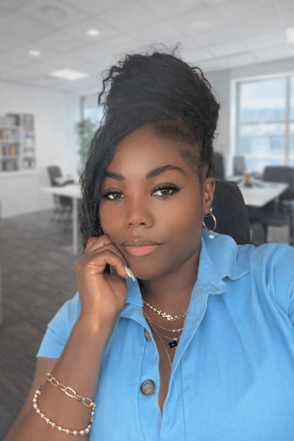 Woman with dark skin and braided bun resting chin on hand wearing a blue shirt.